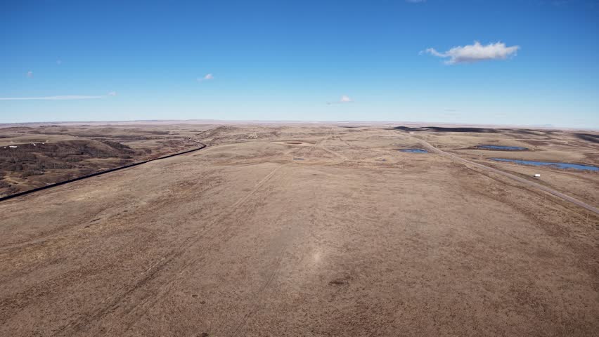 Aerial view of a wide dirt road stretching across barren brown plains beneath a clear blue sky near Whitefish, Montana.