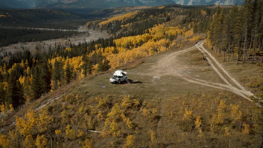 Descending down on a parked Porsche rally-car with a pop-up tent in an Autumn forest environment with a mountain in the distance.