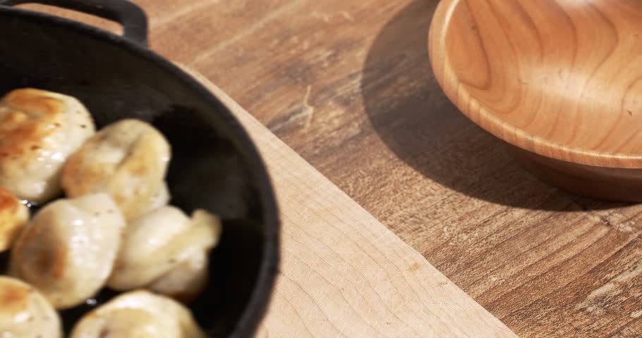Frying pan with freshly fried dumplings is placed on a wooden board, the oil is boiling and steaming.