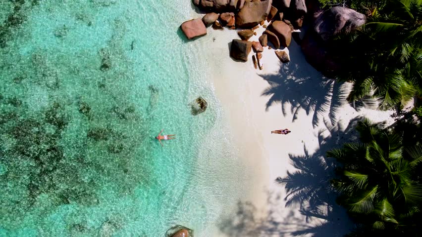 Experience the breathtaking beauty of Anse Lazio in Praslin, Seychelles, where turquoise waters meet soft sandy shores. A diverse couple of a man and woman on the beach during vacation, drone top view
