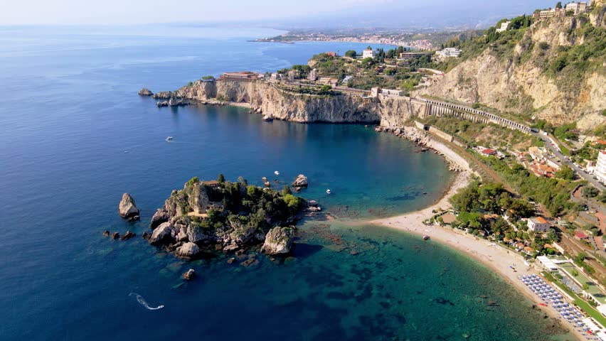 Discover the stunning coastline of Taormina, Sicily, where crystal-clear waters meet rocky cliffs. Enjoy the vibrant beach life and picturesque scenery under the warm sun.
