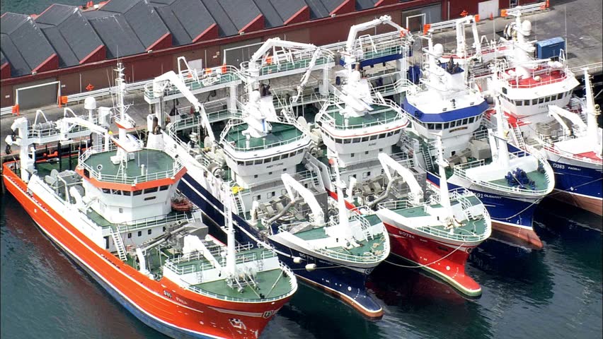 Shows several colorful fishing boats docked closely together at port of Killybegs, Ireland. Daylight view showing industry, maritime activities, and water reflections. marine nature background