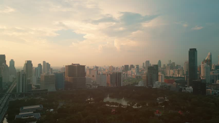 aerial drone view of modern high-rise skyscrapers of Bangkok city and Lumpini green park, financial downtown district top view during sunny sunset, futuristic capital of Thailand 4k