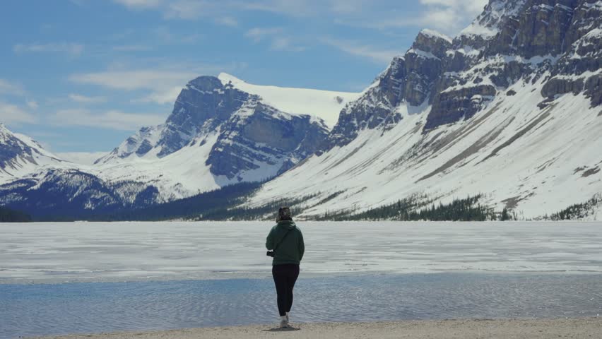 Woman looking out at the partially frozen Bow lake surrounded by snow capped mountains in Banff National Park