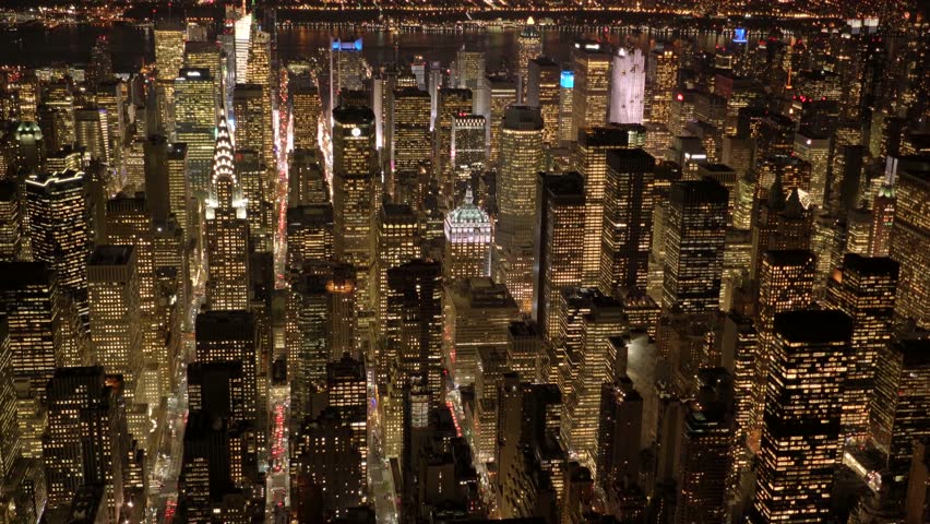 Captivating aerial view of Midtown Manhattan at night, showcasing illuminated skyscrapers lining a bustling avenue with streams of traffic lights below.