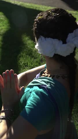 Graceful Latin woman performing classical Indian dance in a park. She turns with a smile, wearing a traditional teal costume and white flower.