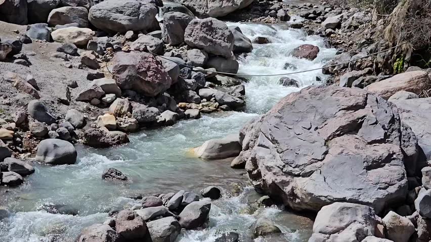 Fast Mountain Stream Running Over Rocks in Summer Mountains. Fast flowing mountain stream rushing over rocks in a bright summer landscape. Dynamic natural scene with fresh water, stones and green plants. Wild alpine environment showing movement and energy of nature. Perfect for themes of mountain river, outdoor adventure, nature background, travel, wilderness and fresh environment.