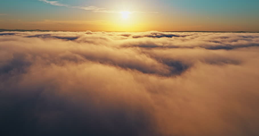 Aerial view drone flight above thick white clouds layer during vibrant golden sunset. Bright sun disk glowing horizon blue sky. Peaceful heaven nature landscape freedom inspiration concept background
