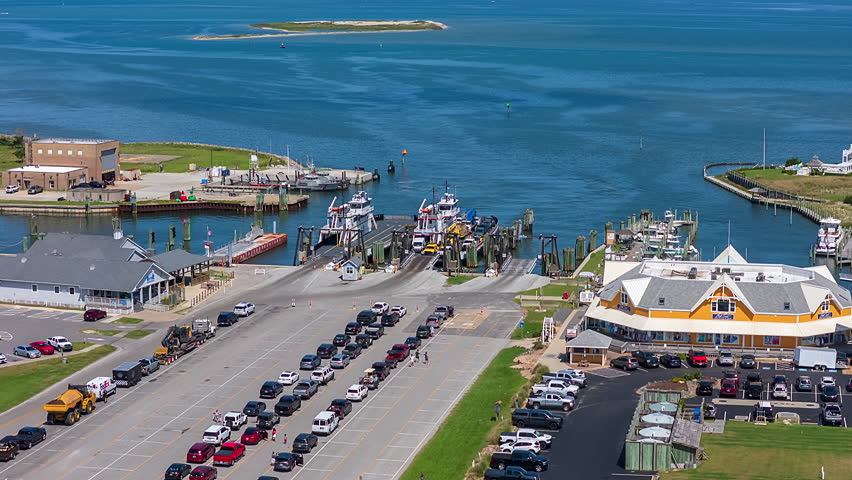 Vehicles Lining Up at a Ferry Terminal in Ocracoke outer banks north carolina Beside Calm Blue Waters, With Docks, Boats, and Waterfront Buildings Surrounding the Harbor - Timelapse