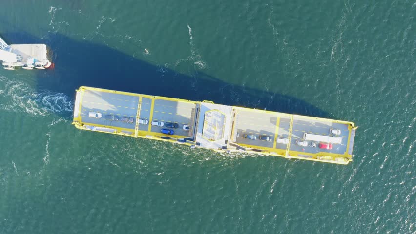 Yellow open deck island car ferry making way ahead in Finnish archipelago. Aerial top down view. Ferry partially loaded with vehicles.