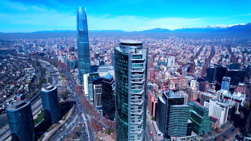 Aerial drone footage capturing the stunning skyline of Santiago, Chile, featuring the iconic Gran Torre Santiago towering over modern skyscrapers, bustling highways, and residential areas.