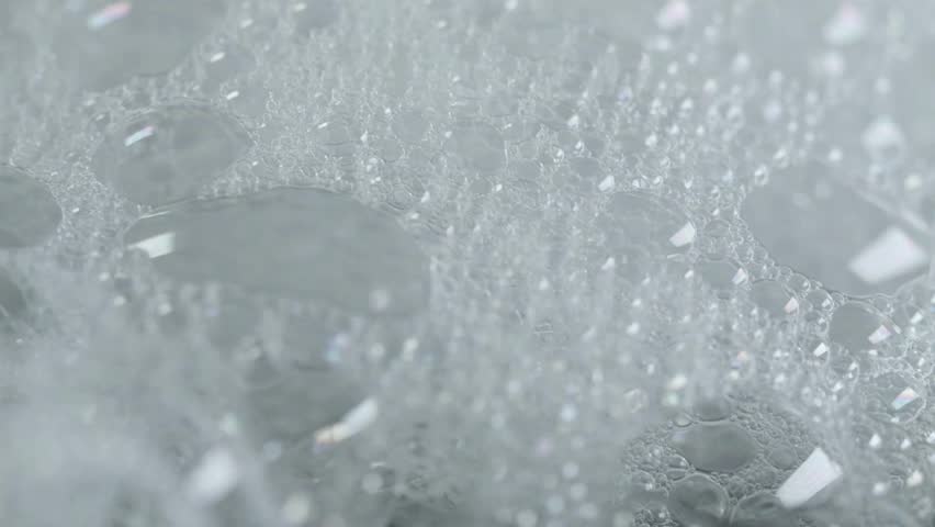 Macro view of white Soap Suds. Bubbles form and pop. Abstract texture and soft white surface. Extreme close up. Liquid moving, foam structure.