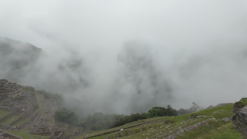 Atmospheric panning shot of the ancient Incan citadel of Machu Picchu covered in thick mist and clouds on a rainy day in the Peruvian Andes