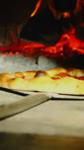 Experienced cook uses special pizza peel to rotate pizza inside stone oven. Chef rotates pizza to achieve uniform cooking. Vertical video