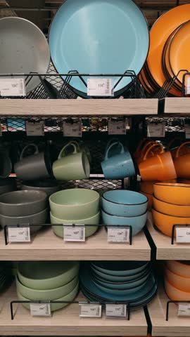 Vertical video of colorful ceramic plates, bowls, and cups on store shelves. Bright kitchen decor, shopping concept, modern tableware and style, home design inspiration. Tableware background