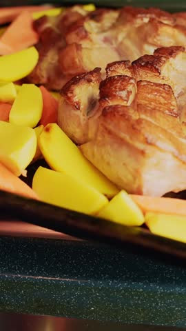 Vertical close-up of roasted chicken pieces with potato wedges and carrots in a baking tray, golden and crispy home-cooked oven dinner with warm comfort food vibes.