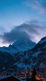 Matterhorn towers over Zermatt, Switzerland, as clouds race by. Snow village lights glow, a hillside cross shines, smoke drifts, and light shifts in a steady vertical frame. - Powered by Shutterstock - Get 15% off with code: PIKWIZARD15