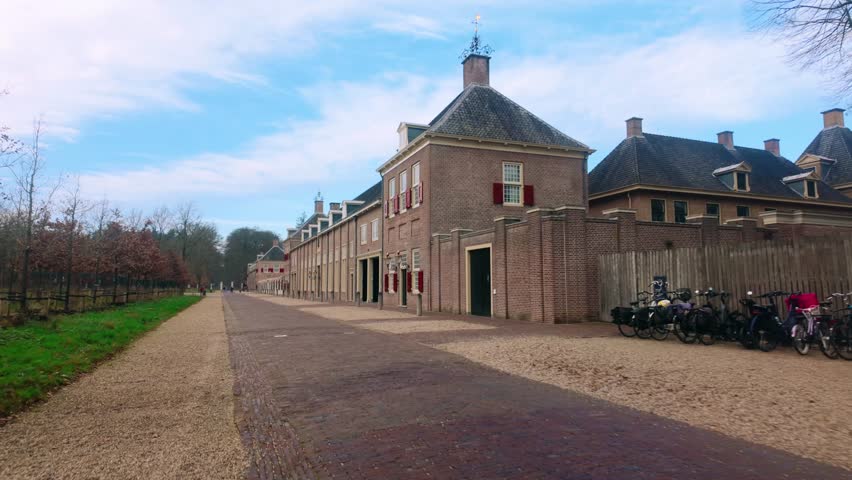 Brick outbuildings and long pathway at Paleis Het Loo royal estate. Traditional Dutch architecture with red shutters. Quiet winter morning at historic palace grounds in Apeldoorn.