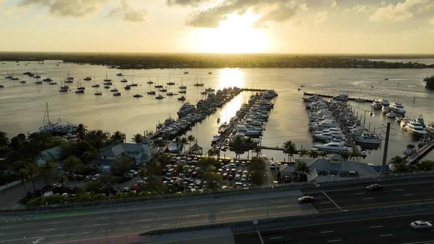 A scenic drone perspective showcases yachts and sailboats resting in the calm waters of Sunset Bay Marina during a Florida sunset.