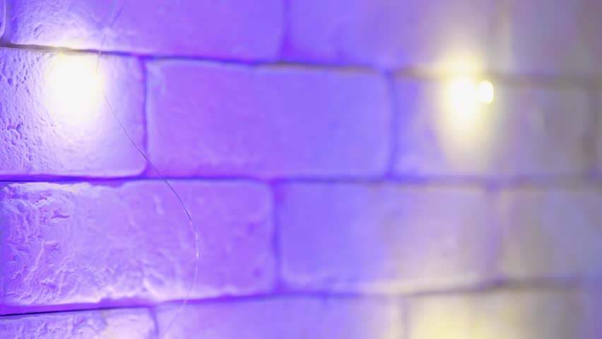 Delicate warm white fairy lights flickering gently along textured stone brick wall bathed in soft blue and purple ambient lighting, creating cozy and calming atmosphere