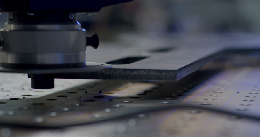Close up of an automated milling tool processing a metal plate with small sparks on a perforated workbench in a factory