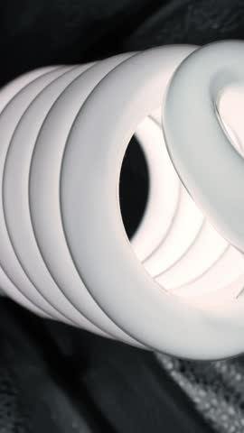 Vertical macro shot of a spiral CFL bulb on a wet dark surface with droplets, shallow depth of field and moody studio lighting.