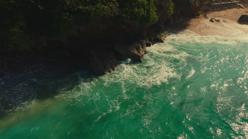 Turquoise ocean waves are crashing against rocky tropical coastline in Bali, Indonesia. Aerial, Circle Dolly