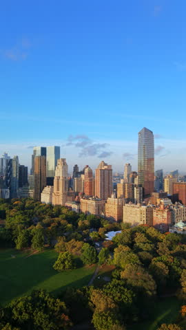 Aerial view of Upper Midtown Manhattan skyline glowing in warm sunlight above Central Park greenery, peaceful city atmosphere with clear sky, New York City, New York