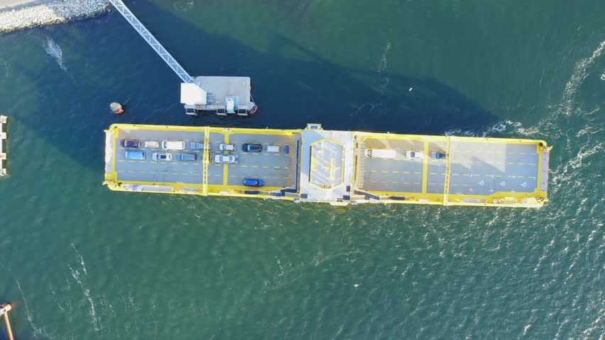 Yellow open deck island car ferry arriving to a road loading ramp in Finnish archipelago. Aerial top down view.