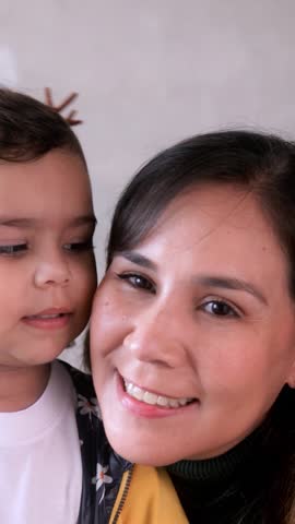 Happy Latin mother and child daughter having tender moment together. Little girl kissing mom - Family love concept. Vertical video
