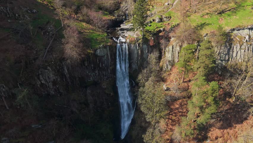 A stationary drone view looking down on the top of the fast flowing Pistyll Rhaeadr waterfall in Powys, Wales during Springtime.