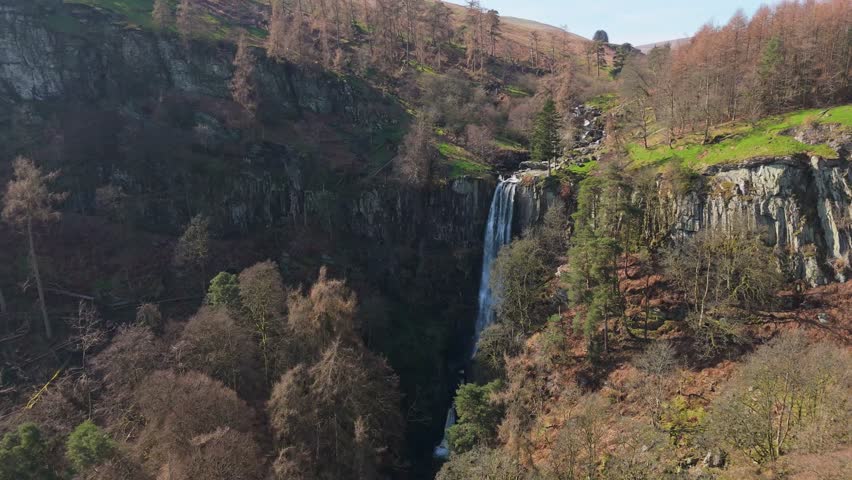 A close high drone orbit view of the impressive Pistyll Rhaeadr waterfall looking down amongst the vegetation in Powys, Wales, UK