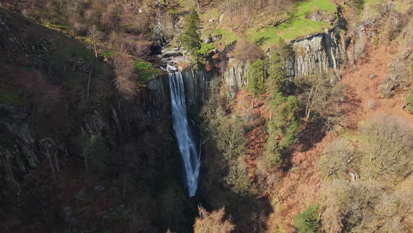 A close high drone orbit view of the impressive Pistyll Rhaeadr waterfall looking down amongst the vegetation in Powys, Wales, UK