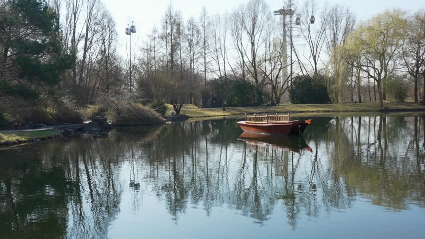 A small wooden boat floats on a calm lake reflecting trees and sky in a peaceful park landscape.