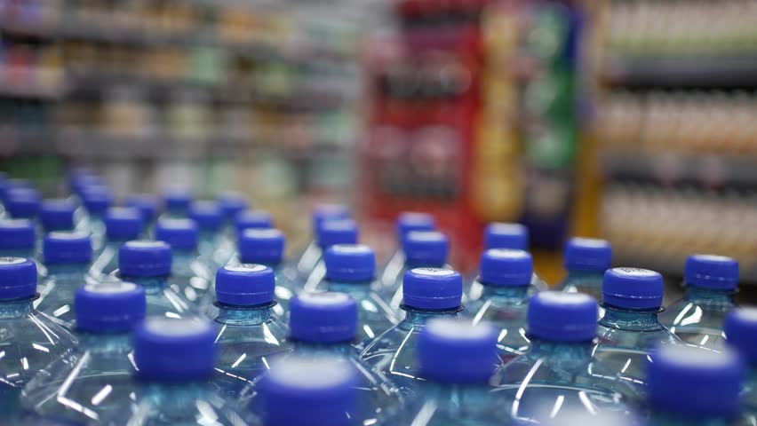 Close-up of a female hand choosing and taking a plastic bottle of pure drinking water from a store shelf, highlighting the concept of making a healthy lifestyle choice in a supermarket
