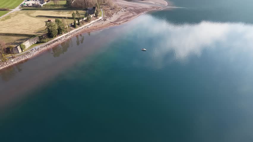 Drone orbiting 180 degrees around a fisherman in a small boat on a quiet lake. Calm water and peaceful outdoor fishing scene.