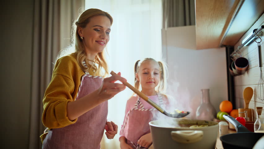 Parent child sniffing soup aroma cooking at kitchen together closeup. Young family preparing tasty dinner at warm light home. Mother daughter enjoying making lunch indoors. Cute girl helping mom
