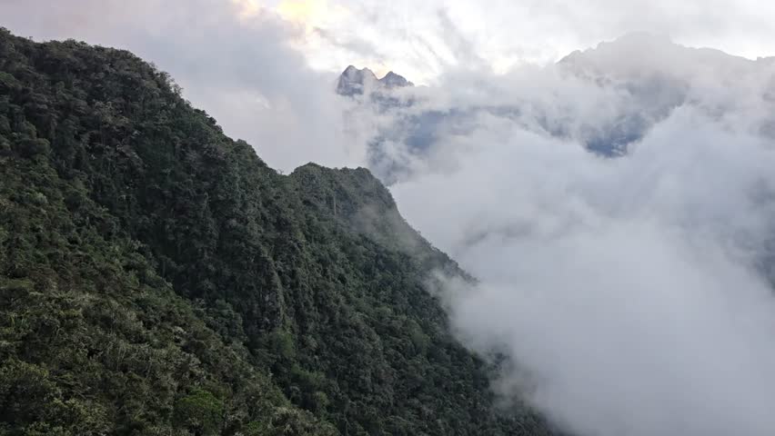 Andes Mountains, Peru - 26 June 2024. Thick cloud cover moving across rugged mountain peaks, obscuring slopes and revealing sharp ridges beneath a grey sky.