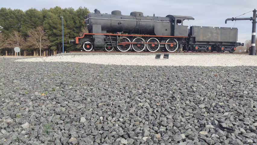 Old steam locomotive standing as a monument on a gravel roundabout under a cloudy sky