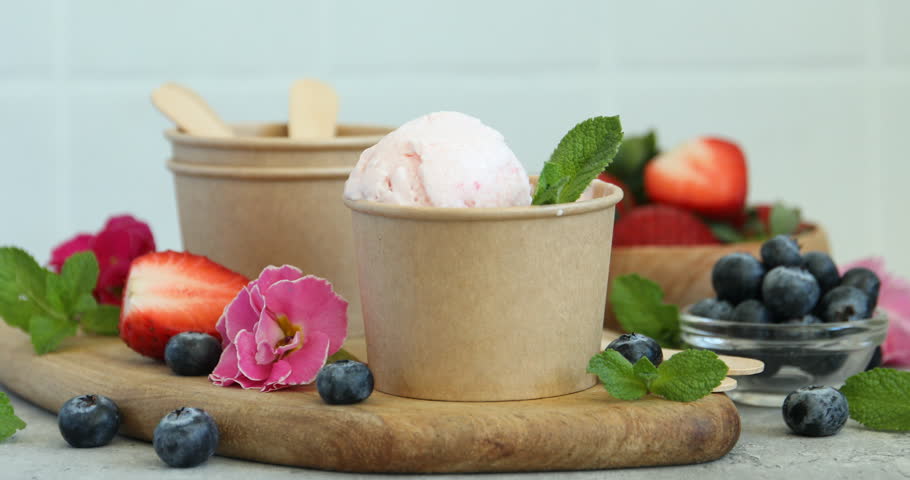 Woman adding strawberry to tasty frozen yogurt at light table, closeup