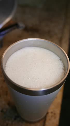 Close-up of bubbles bursting in beer foam. A glass of beer on the table. A beer tumbler. A beer cup. An insulated cup. An insulated tumbler. A mug. A frothy drink.