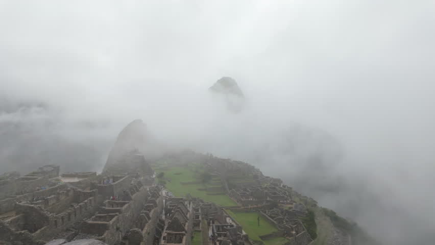 Atmospheric panning shot of the ancient Incan citadel of Machu Picchu covered in thick mist and clouds on a rainy day in the Peruvian Andes