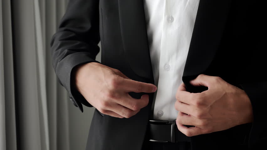 Close up of man buttoning suit jacket preparing for business meeting or formal event in clean minimal interior.