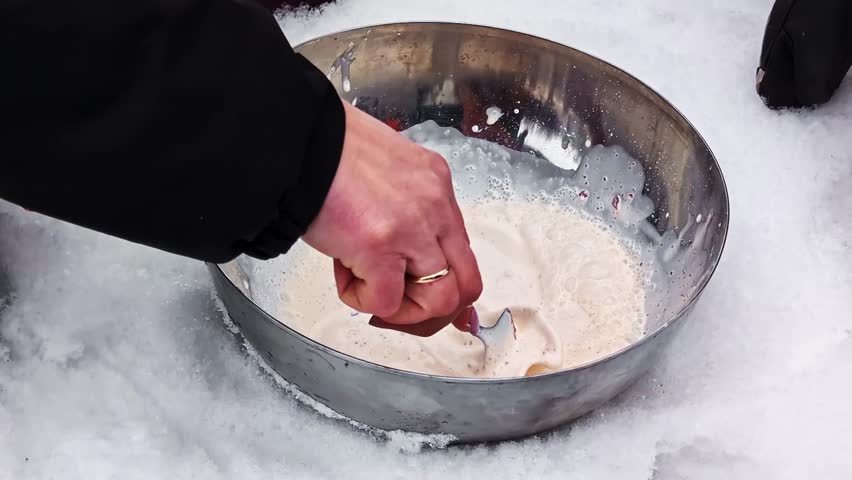 Person mixing sweet cream in metal bowl, making ice cream during winter outdoors