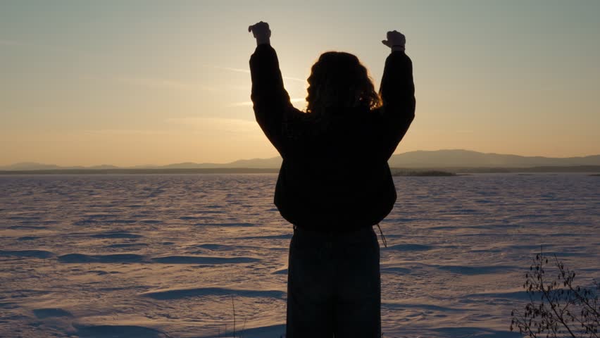 A happy young girl holds out her arms to the sun at sunset. The girl is enjoying life. Love of nature and inspiration. Rear view.	