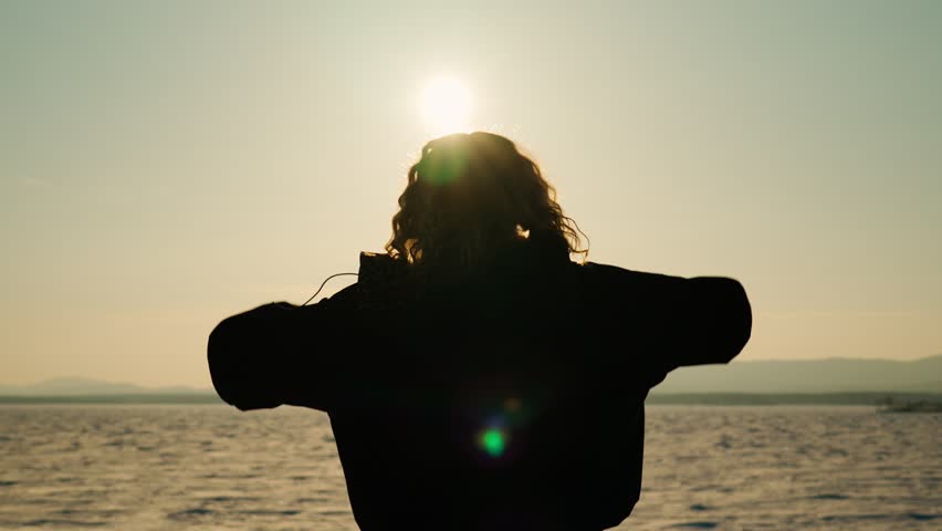 A happy young girl holds out her arms to the sun at sunset. The girl is enjoying life. Love of nature and inspiration. Rear view.	