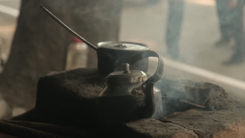 Closeup video of a metal tea kettle boiling on a traditional wood fire stove. Rural cooking scene with smoke, heat, and authentic village lifestyle atmosphere.
