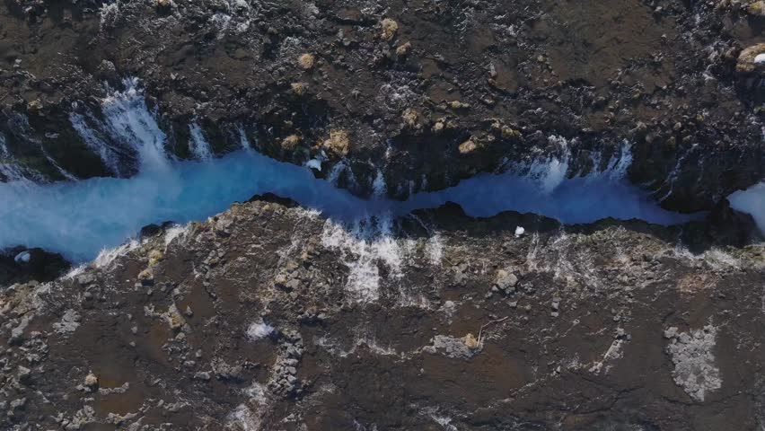 Top down sliding right as narrow Bruarfoss river widens into rapids, Iceland