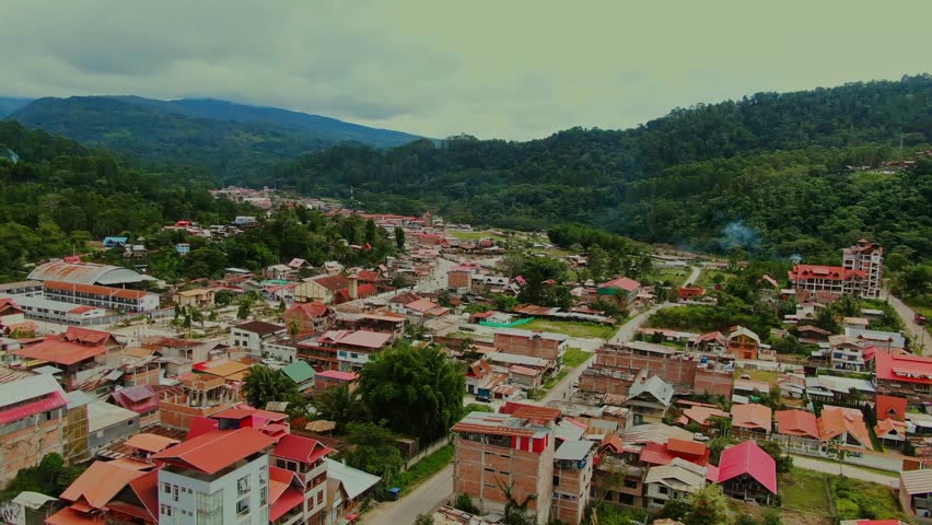 Aerial drone view moving forward over the misty city of Villa Rica, Peru, showing residential houses and a main avenue surrounded by cloudy high jungle mountains.