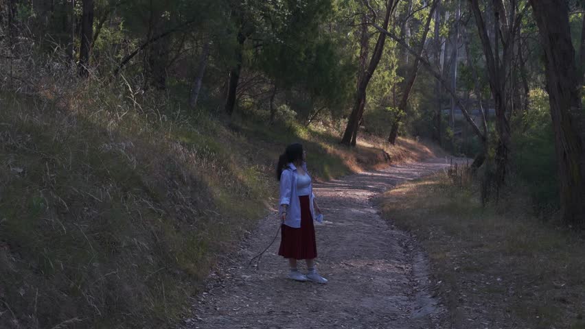 A girl throws a stick along a twilight forest path in Warrandyte Park, Melbourne. The evening sun casts a warm glow, enhancing the tranquil natural landscape.